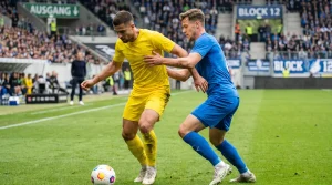 Zwei Profi-Fußballer in unterschiedlichen Trikots im direkten Zweikampf um den Ball auf dem grünen Rasen eines Bundesliga-Stadions
